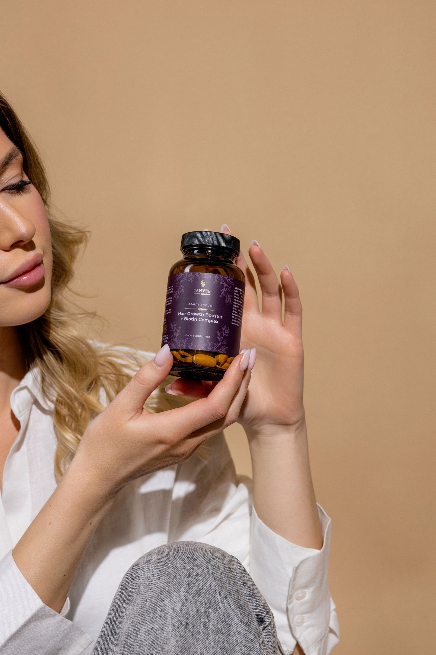 Woman holding Sanvee hair growth booster with biotin bottle against neutral background