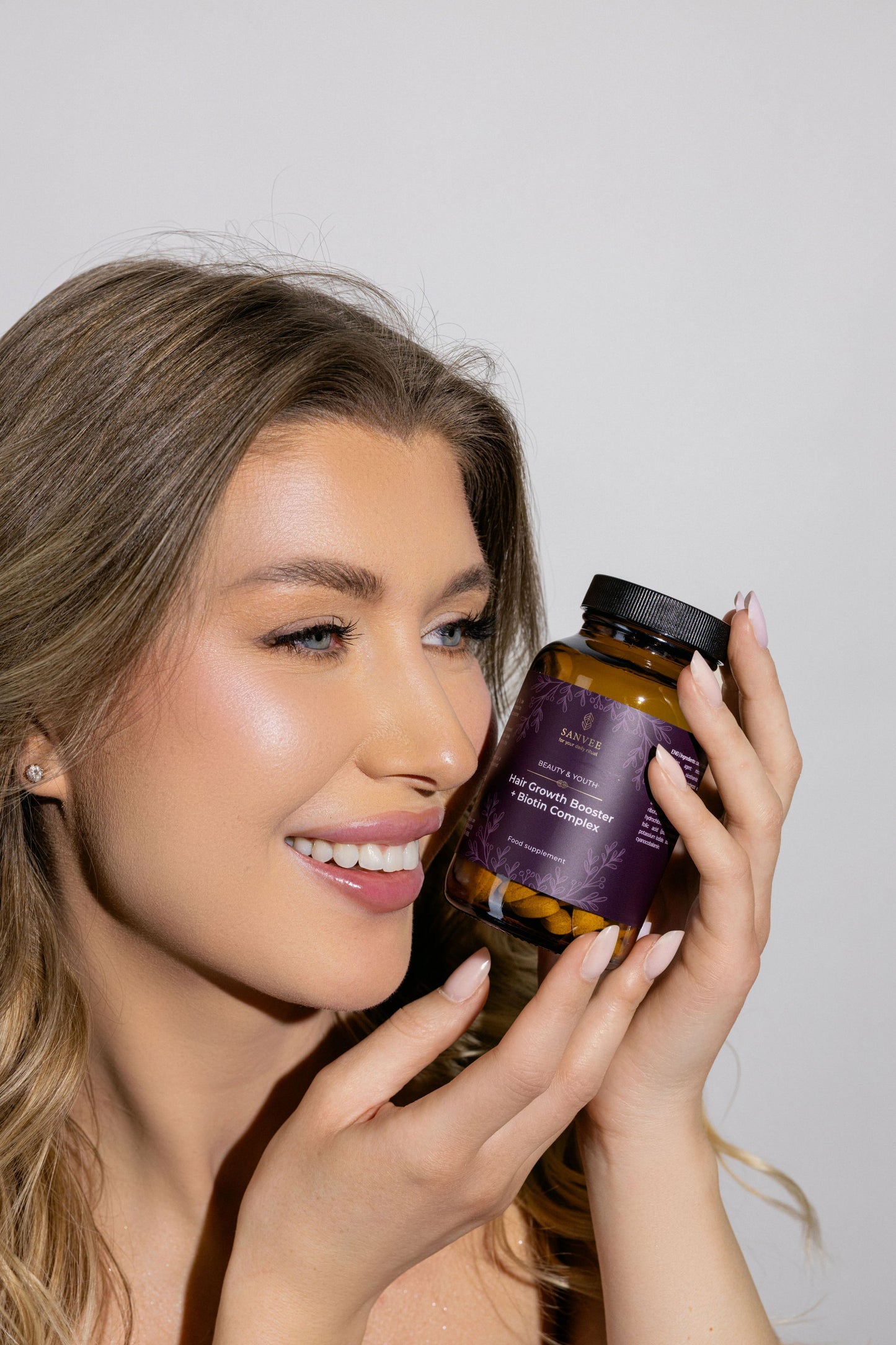 Woman holding Sanvee hair growth booster biotin supplement bottle near face