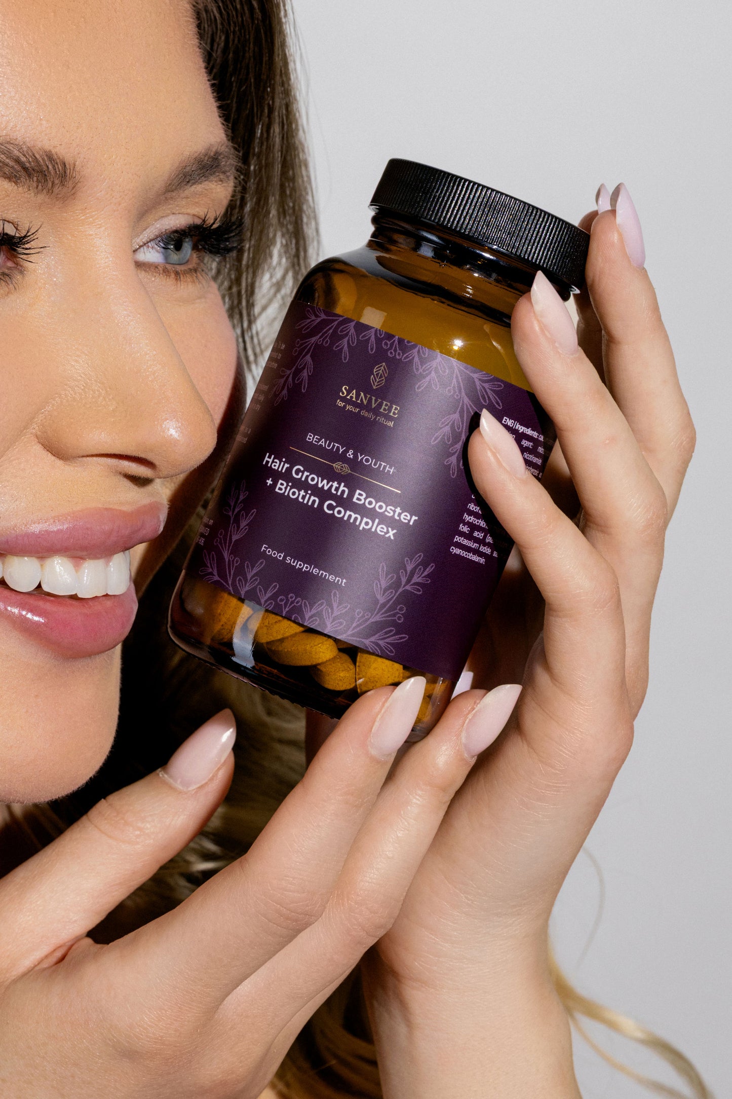 Woman holding Sanvee hair growth booster with biotin bottle near face