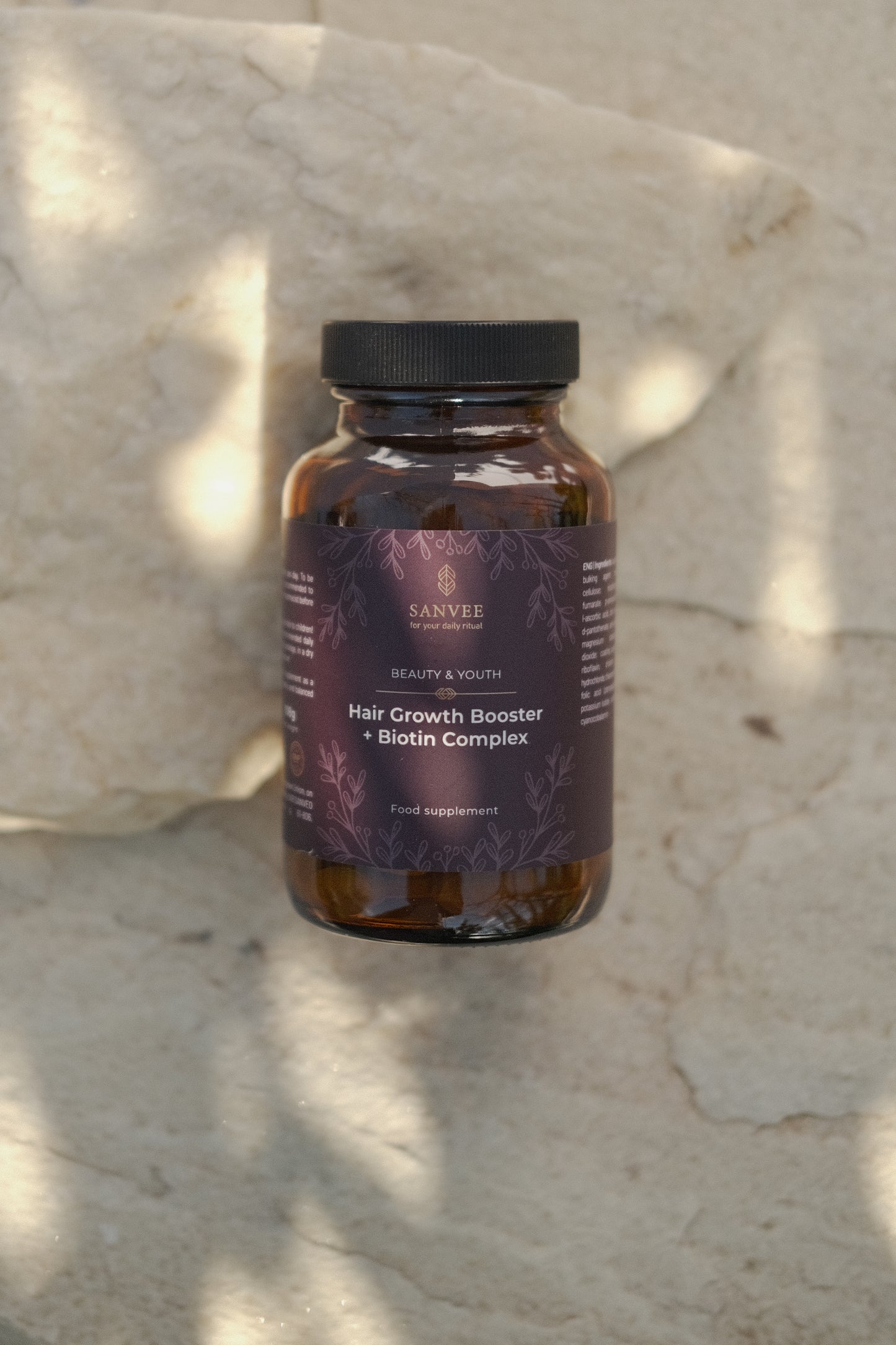 Sanvee hair growth booster with biotin bottle on stone surface in natural light